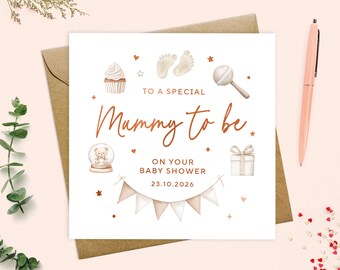 May include: A white greeting card with the text "To a special Mummy to be" in a copper color, with baby-themed illustrations. The card is on a brown envelope, with a pink pen and decorative elements.