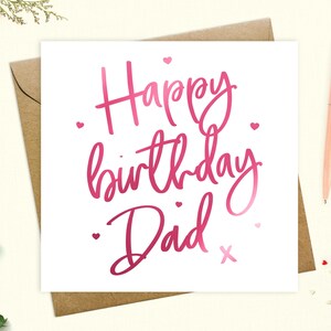 May include: A white card with pink foil lettering that says "Happy birthday Dad" with a pink heart and an X at the end of the text.