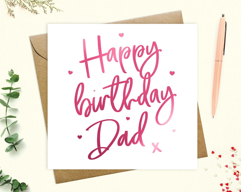 May include: A white card with pink foil lettering that says "Happy birthday Dad" with a pink heart and an X at the end of the text.