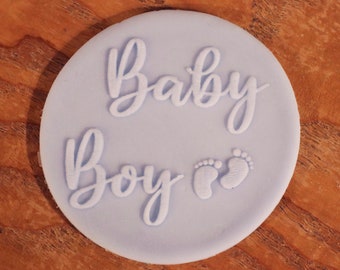 May include: A light blue round cake topper with the words "Baby Boy" in white script and two white footprints.
