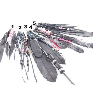 Puede incluir: Cinco llaveros de plumas de cuero negro con diferentes cuentas y abalorios. Los abalorios incluyen cuentas rosas, cuentas plateadas y pequeños abalorios de metal con la palabra "GIRL" en ellos.