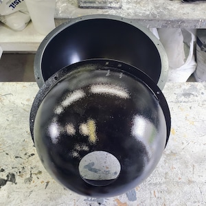 May include: Two black, round, dome-shaped objects with a hole in the center. The larger dome is sitting on top of the smaller dome.