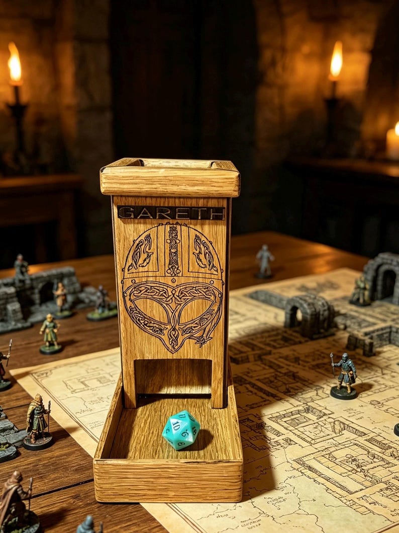 May include: A light brown wooden dice tower featuring a laser-engraved Viking helmet design and the name GARETH etched at the top. The tower has an open front tray where a single turquoise twenty-sided die rests on the flat wooden surface.