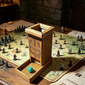 May include: A wooden dice tower with a square top opening and a front tray featuring a carved helmet design. A single turquoise twenty-sided die rests in the tray. The tower is positioned on a game board with various miniature figures and paper maps.
