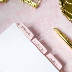 May include: Pink tab dividers for a planner or notebook with the months January, February, and March printed on them.