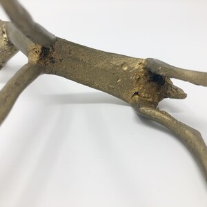 May include: A gold-colored metal sculpture of a stylized animal, possibly a deer or antelope, with its legs outstretched. The sculpture is in a leaping pose, with its head tilted back.