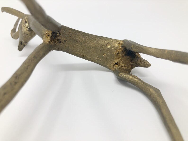 May include: A gold-colored metal sculpture of a stylized animal, possibly a deer or antelope, with its legs outstretched. The sculpture is in a leaping pose, with its head tilted back.