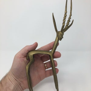May include: A gold-colored metal sculpture of an antelope with long, twisted horns. The sculpture is standing on a flat surface.