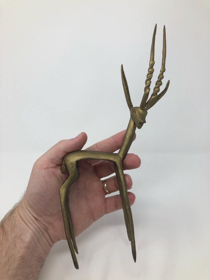 May include: A gold-colored metal sculpture of an antelope with long, twisted horns. The sculpture is standing on a flat surface.