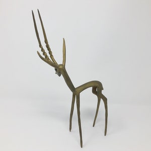 May include: A gold-colored metal sculpture of an antelope with long, twisted horns. The sculpture is stylized and abstract, with a minimalist design.