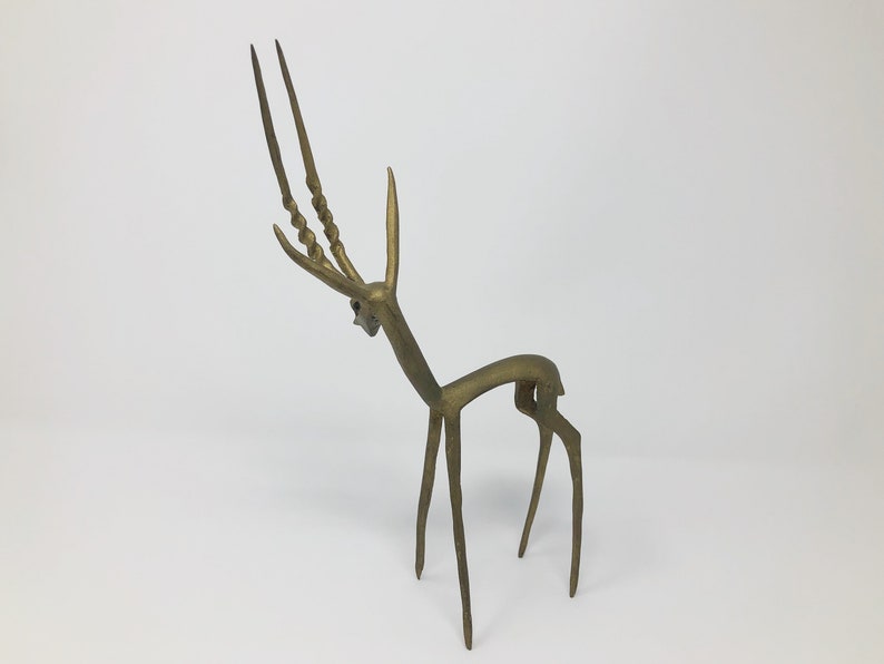 May include: A gold-colored metal sculpture of an antelope with long, twisted horns. The sculpture is stylized and abstract, with a minimalist design.