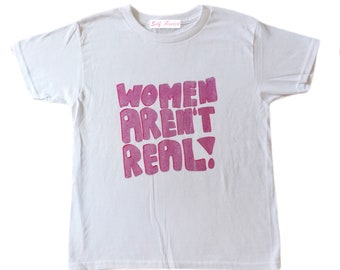 May include: White t-shirt with pink lettering that reads "Women Aren't Real!" The shirt has a small tag that reads "Self Creative".