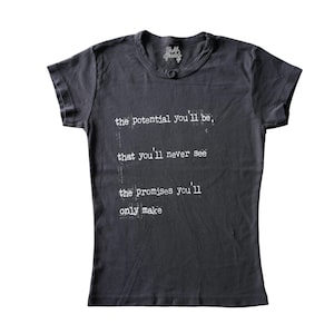 May include: A dark gray short-sleeved t-shirt featuring white typewriter-style text on the front that reads: the potential you'll be, that you'll never see, the promises you'll only make. The shirt has a round neckline and a small brand logo inside.