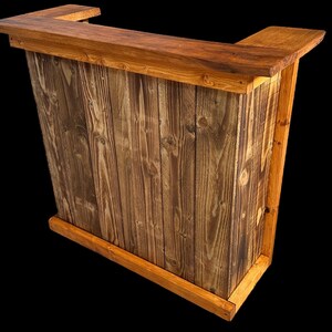 Op de afbeelding: Een houten bartafel met een rustieke bruine afwerking en een natuurlijke houtnerf. De tafel heeft een rechthoekig blad en een verhoogde rand. De voorkant van de tafel is gemaakt van verticale houten planken.