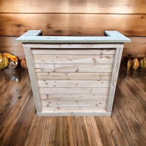 May include: A wooden counter with a light wood finish and a natural wood grain. The counter has a simple design with a rectangular top and a base made of horizontal planks.