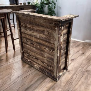 May include: A rustic wooden bar counter with a dark brown finish and a natural wood grain pattern. The counter has a rectangular shape and a simple design.