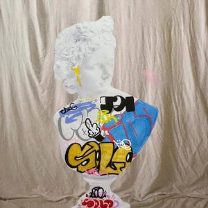 Könnte beinhalten: Eine weiße Gipsbüste einer Frau mit Graffiti bemalt. Die Graffiti beinhalten die Wörter "ICE", "GO" und "SALE" in verschiedenen Farben.