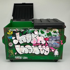 May include: A green metal dumpster with a black lid. The dumpster is covered in graffiti, including the words "Crush It" and "Go Big Lou!"