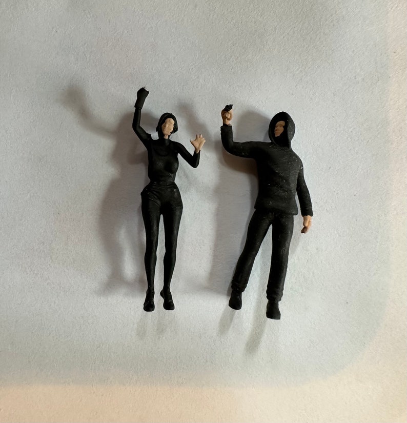 May include: Two black figurines, one with a raised arm and the other holding a small object in their hand.