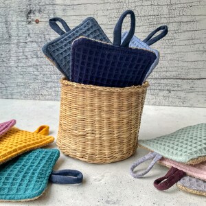 May include: A set of colorful waffle weave pot holders with a woven basket. The pot holders are in shades of blue, green, yellow, and pink.