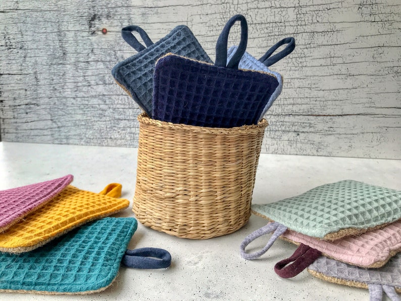 May include: A set of colorful waffle weave pot holders with a woven basket. The pot holders are in shades of blue, green, yellow, and pink.