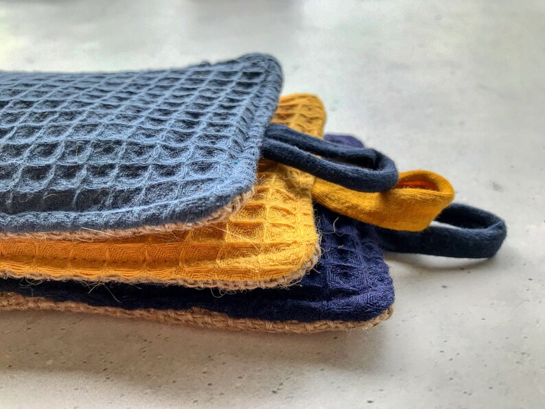 May include: Three kitchen dishcloths stacked on top of each other. The top dishcloth is blue, the middle dishcloth is yellow, and the bottom dishcloth is blue.