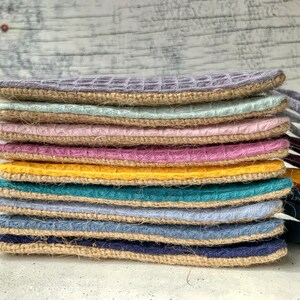 May include: A stack of ten colorful pot holders with a woven texture and a burlap trim. The pot holders are in shades of gray, light blue, pink, purple, yellow, teal, and blue.