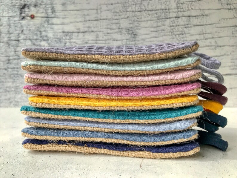 May include: A stack of ten colorful pot holders with a woven texture and a burlap trim. The pot holders are in shades of gray, light blue, pink, purple, yellow, teal, and blue.