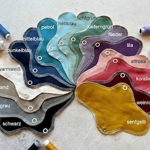 Peut inclure: Un nuancier de tissus de diff&eacute;rentes nuances de bleu, vert, rose, rouge, jaune, marron et gris. Les &eacute;chantillons sont dispos&eacute;s en cercle avec les noms des couleurs &eacute;crits en allemand.