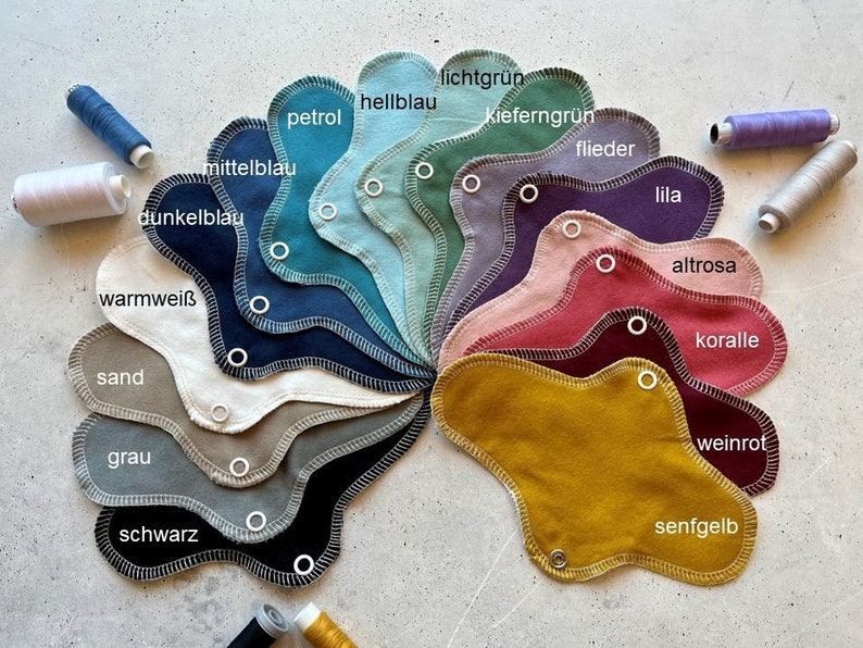 Peut inclure: Un nuancier de tissus de diff&eacute;rentes nuances de bleu, vert, rose, rouge, jaune, marron et gris. Les &eacute;chantillons sont dispos&eacute;s en cercle avec les noms des couleurs &eacute;crits en allemand.