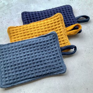 May include: Three waffle weave kitchen pot holders. One is yellow, and two are blue.