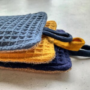 May include: Three kitchen dishcloths stacked on top of each other. The top dishcloth is blue, the middle dishcloth is yellow, and the bottom dishcloth is blue.