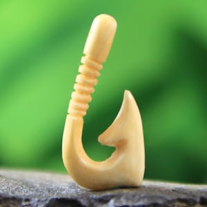 以下が含まれることがあります： 詳細なデザインが施された、木製の釣り針の彫刻。釣り針は薄い茶色の木で作られており、滑らかで磨かれた仕上げになっています。