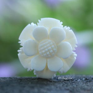 Puede incluir: Un anillo de hueso tallado en forma de flor blanca. La flor tiene cinco pétalos y un centro detallado.