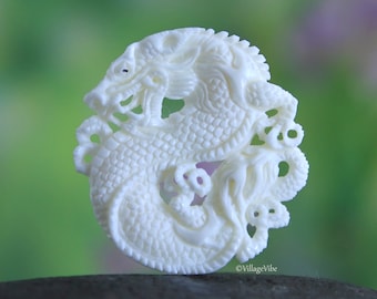 May include: White carved bone dragon pendant with intricate details. The dragon is curled in a circle with its tail in its mouth.