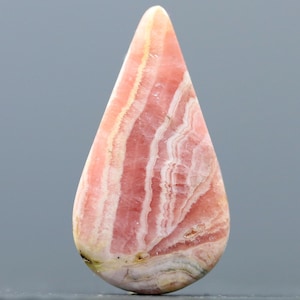 May include: A teardrop-shaped pink and white banded gemstone cabochon. The stone has a smooth, polished surface and is translucent.