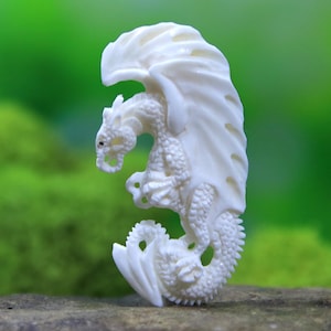 May include: A detailed, ivory-colored dragon figurine with outstretched wings. The dragon is carved with intricate scales and features, including a detailed head, claws, and a curled tail. The wings are large and flowing, adding to the fantasy theme.