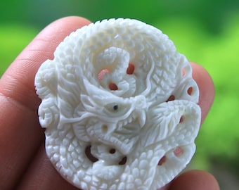 May include: A white carved dragon pendant made from bone. The dragon is curled up in a circle with its head facing forward. The pendant is detailed with intricate carvings.