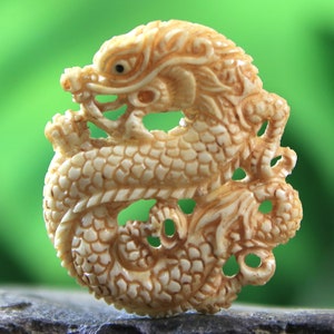 May include: A detailed ivory carving of a dragon curled into a circle. The dragon is intricately carved with scales and claws, and its eyes are inlaid with black.