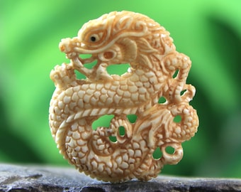 May include: A detailed ivory carving of a dragon curled into a circle. The dragon is intricately carved with scales and claws, and its eyes are inlaid with black.