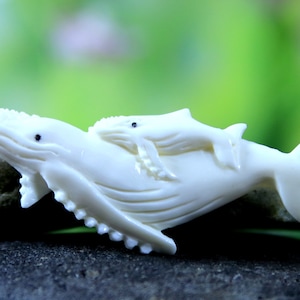 May include: A white whale carving with a smaller whale carved on top. Both whales have black eyes.