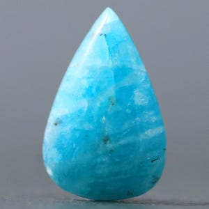 May include: A teardrop-shaped cabochon of blue amazonite gemstone. The stone has a light blue color with white and gray streaks throughout.