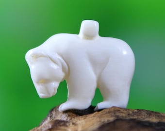 May include: A white carved bear figurine with a small hole on top for hanging. The bear is standing on a piece of wood.