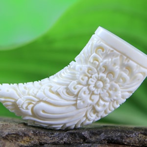 Op de afbeelding: Een wit gegraveerd beenhanger met een bloemmotief. De hanger is gevormd als een gebogen hoorn.