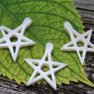 May include: Three white, intricately carved, five-pointed star shapes with a geometric design. The stars are made of a smooth, white material and are arranged on a green leaf.