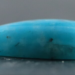 May include: A smooth, teardrop-shaped turquoise cabochon with a light blue color and dark brown inclusions.
