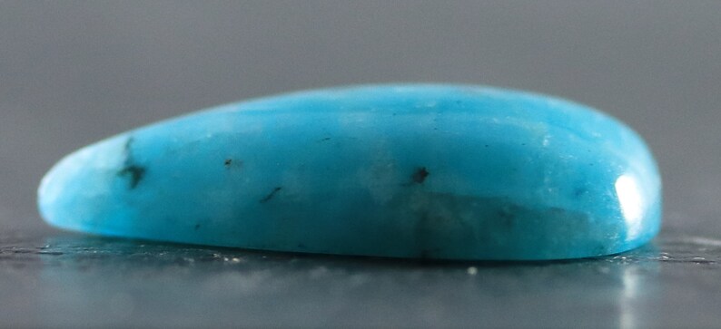 May include: A smooth, teardrop-shaped turquoise cabochon with a light blue color and dark brown inclusions.