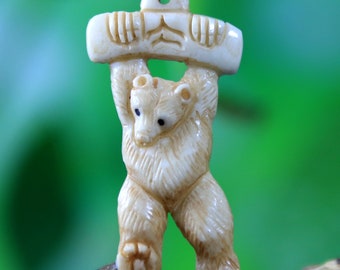 May include: A carved ivory pendant of a bear holding a log above its head. The bear is standing on its hind legs and has a detailed face.