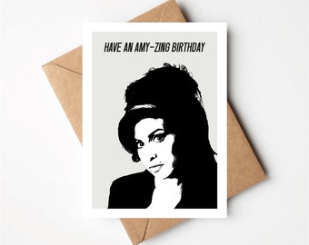 May include: A white card with black text that reads "Have an Amy-Zing Birthday". A black and white illustration of Amy Winehouse is on the card.