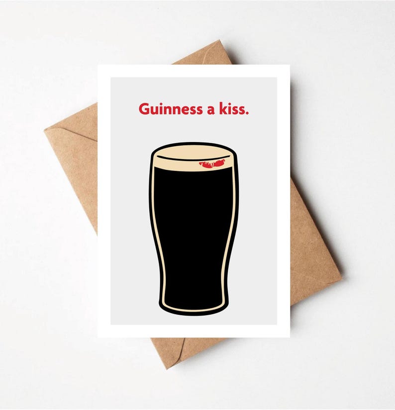 May include: Greeting card with a cartoon illustration of a pint of Guinness with a kiss mark on the foam. The text "Guinness a kiss" is above the pint in red. The card is on a white background with a brown envelope.